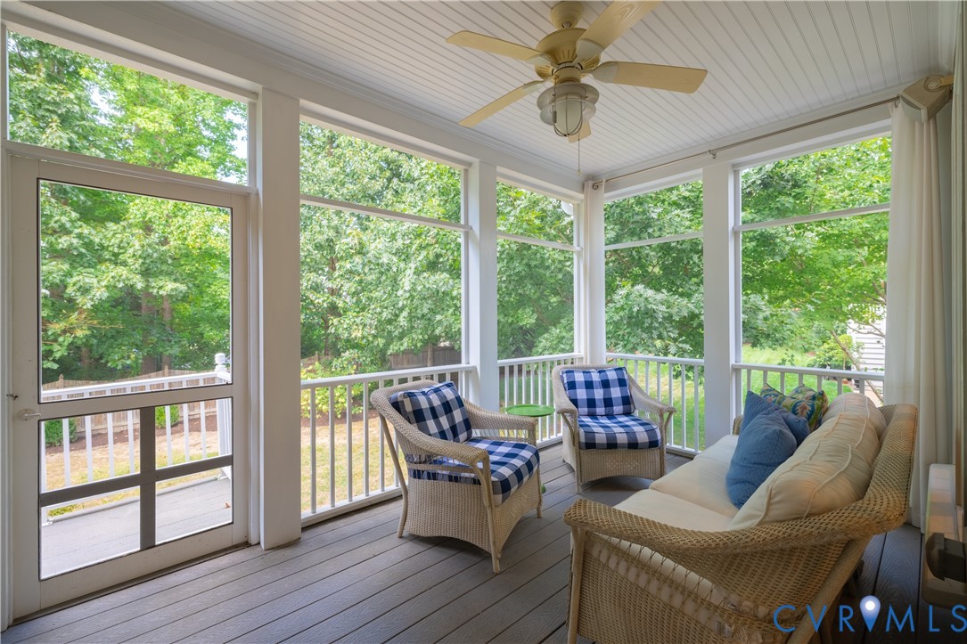 Enclosed porch with wicker seating, broad windows, and leafy trees outside.