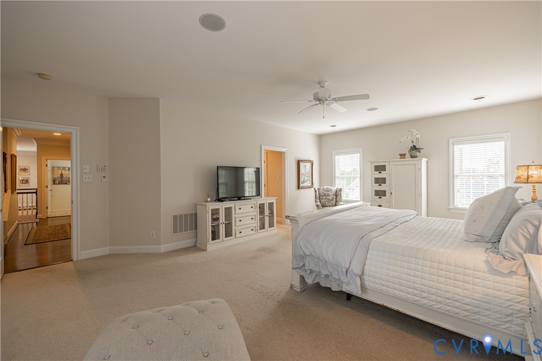 Furnished bedroom with a large white bed, beige carpet, and ceiling fan.