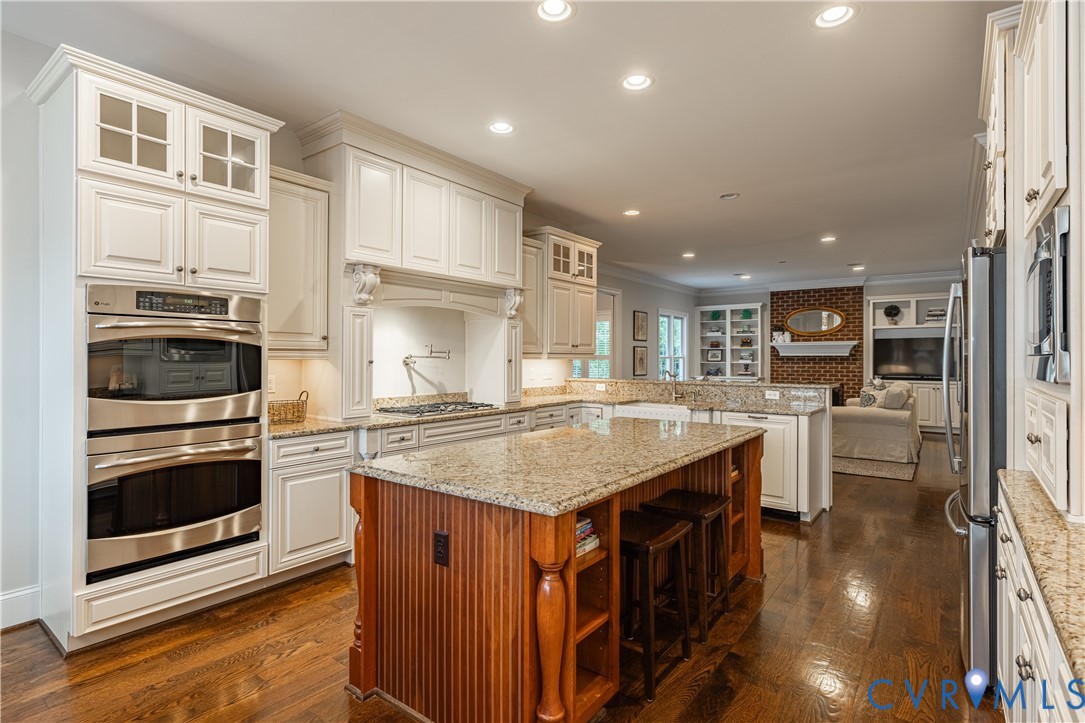 Kitchen with white cabinetry, granite counters, double wall ovens, and a large wood-paneled island.