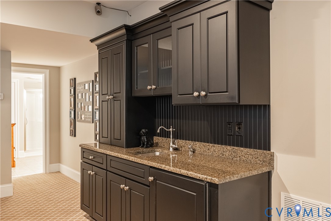 Built-in wet bar with dark cabinets, glass-front cupboards, and a speckled stone countertop.