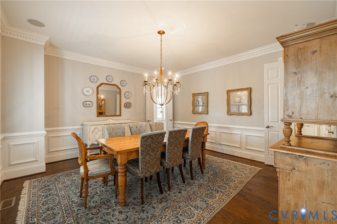 Formal dining room with a wooden table, upholstered chairs, chandelier, and patterned rug.