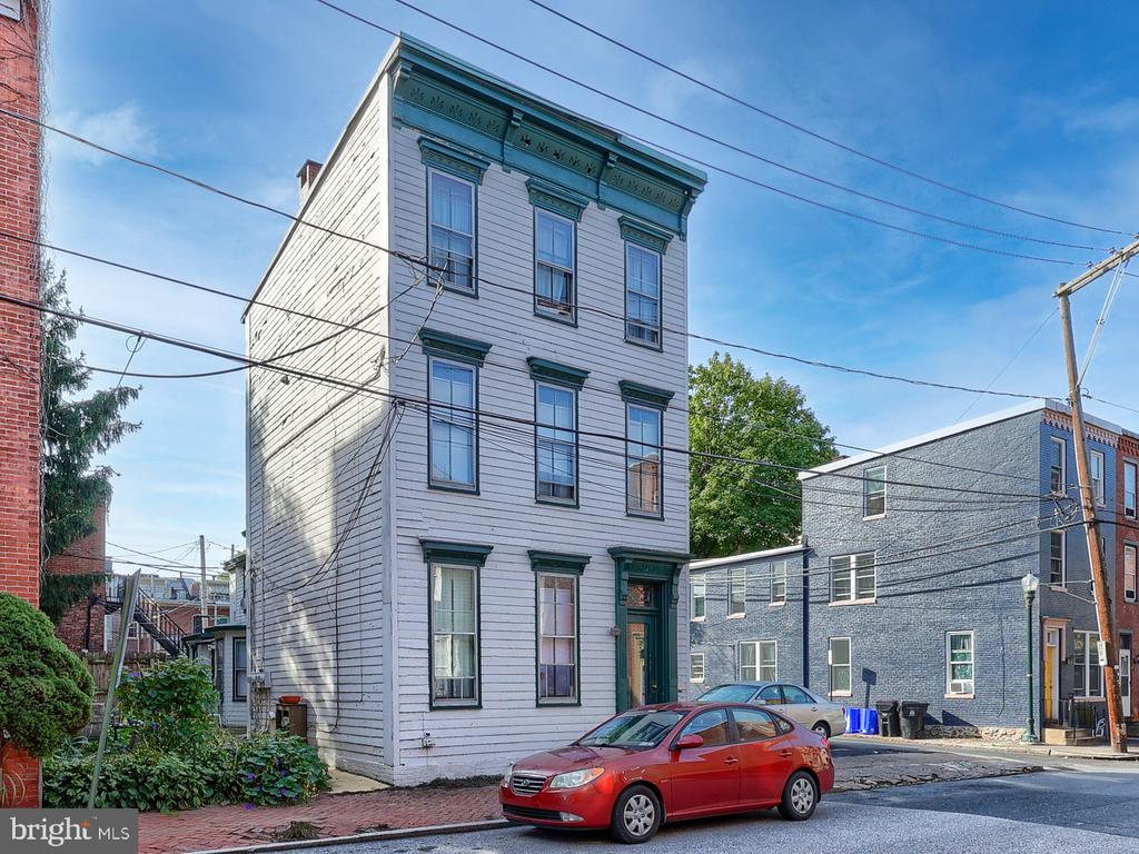 Three-story white-sided house with dark green trim on an urban street.