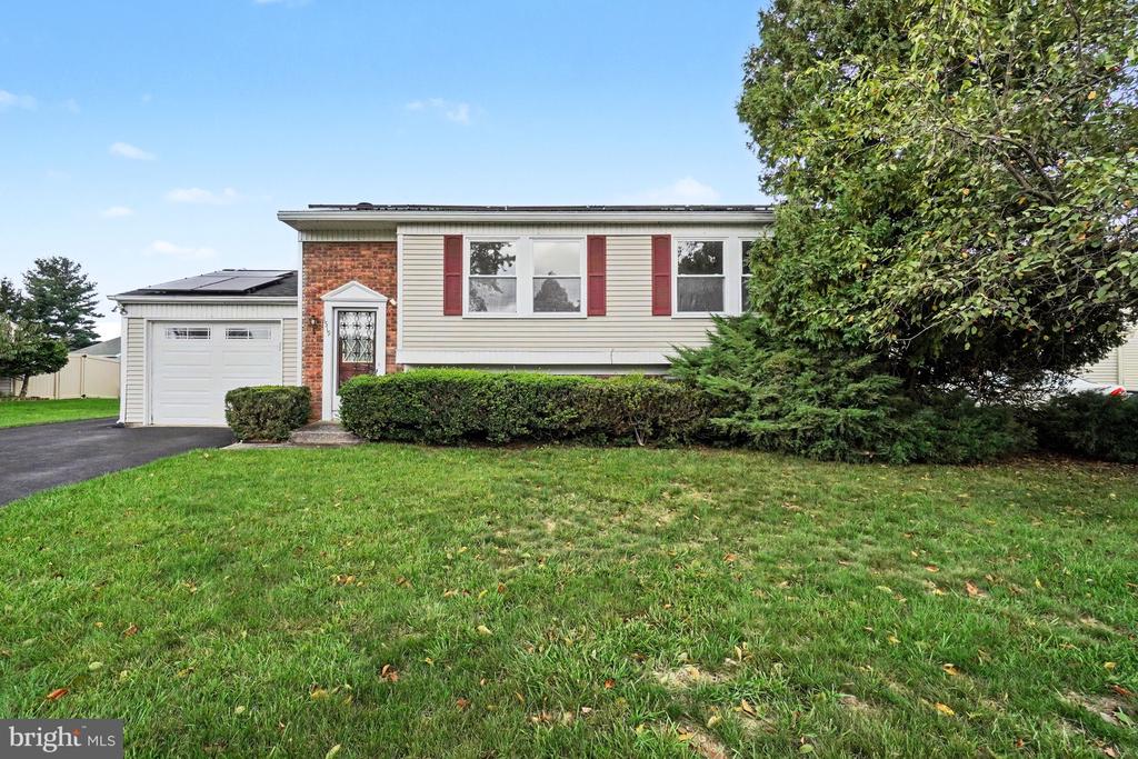 Split-level house with red shutters, brick facade, solar panels, and an attached garage.