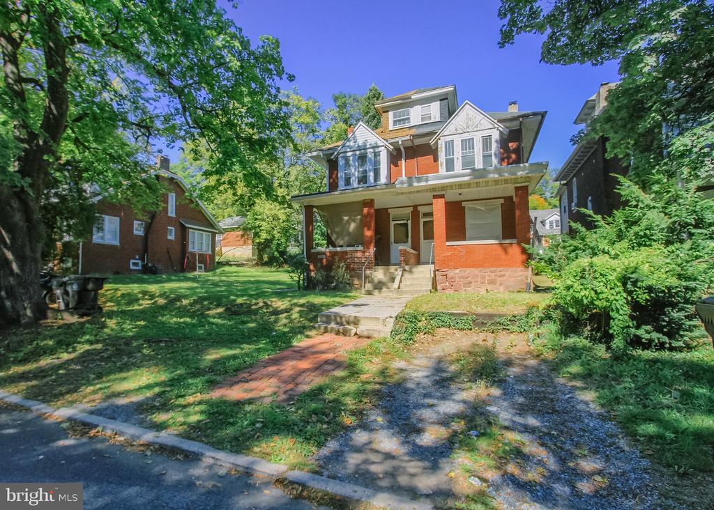Multi-story brick and white house with a covered porch and leafy front yard.