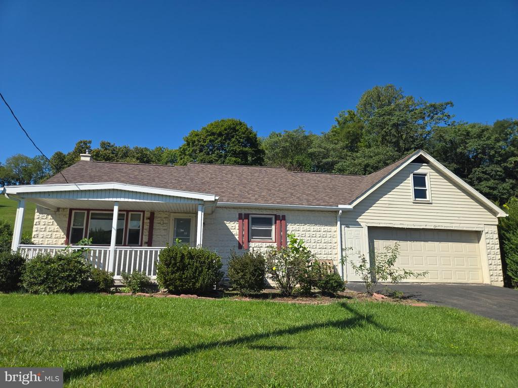 Ranch home with a stone facade, covered porch, attached garage, and broad front lawn.