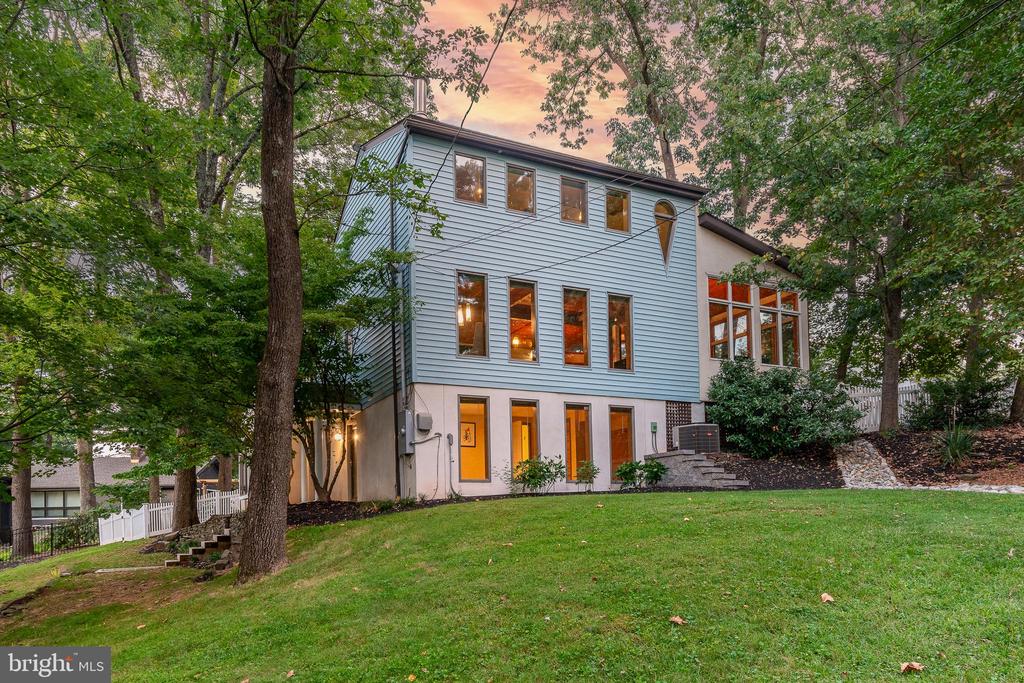 Modern pale blue house with tall windows nestled among mature trees on a sloping lawn.