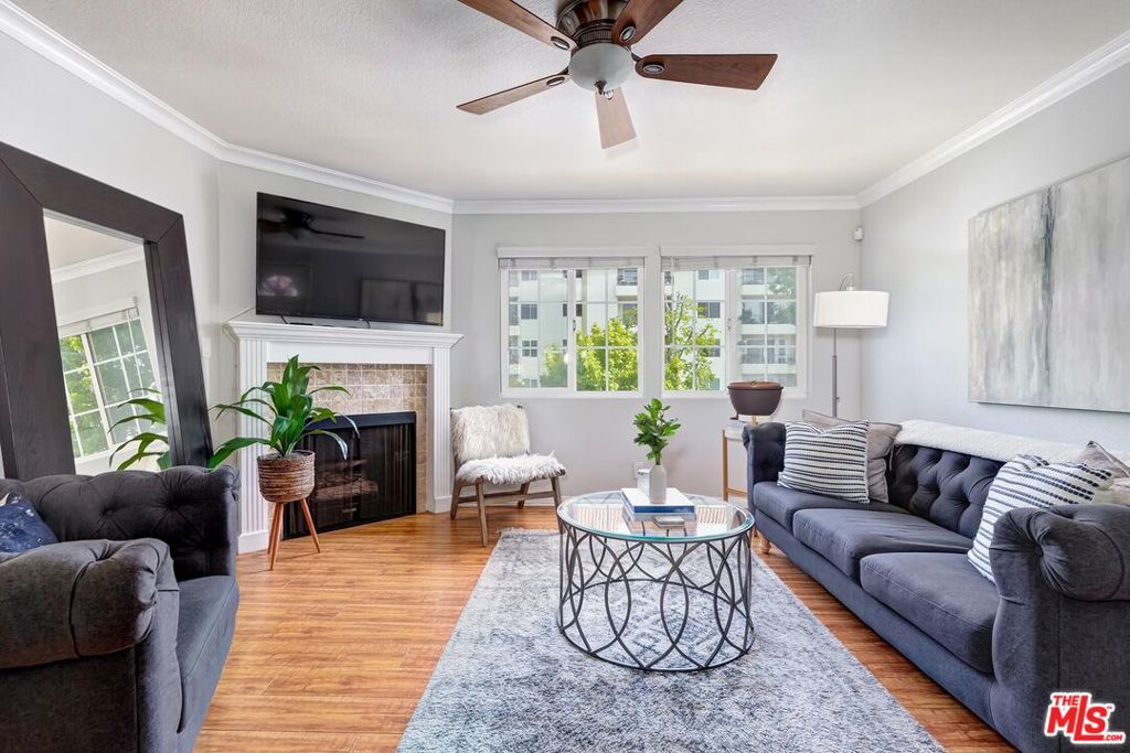 Furnished living room with a white fireplace, dark sofas, large windows, and a round glass coffee table.