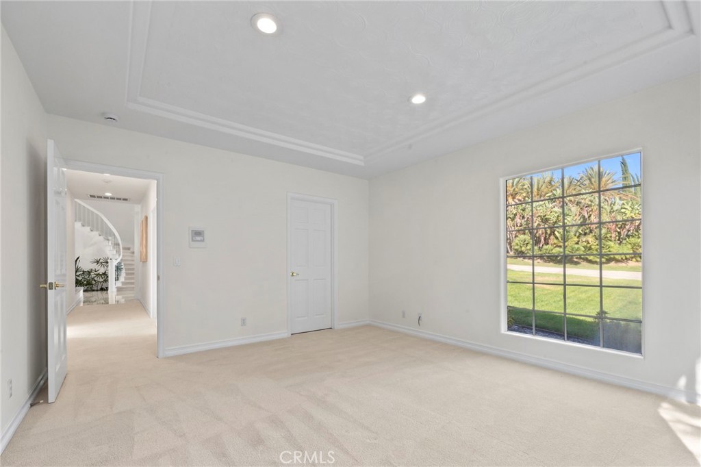 Empty carpeted room with a decorative recessed ceiling and large window overlooking a lawn and palm trees.