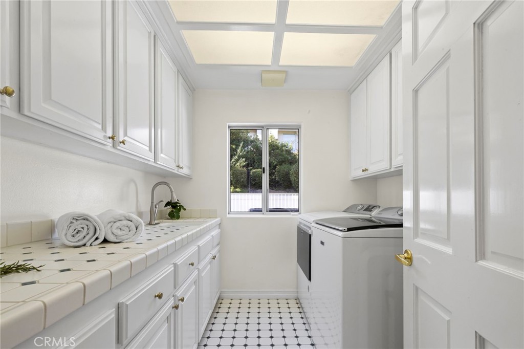 Laundry room with white cabinetry, tiled sink counter, washer and dryer, and patterned floor tile.