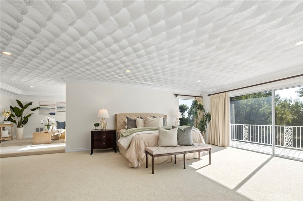 Staged bedroom with a sculptural white ceiling and sliding glass doors to a balcony.