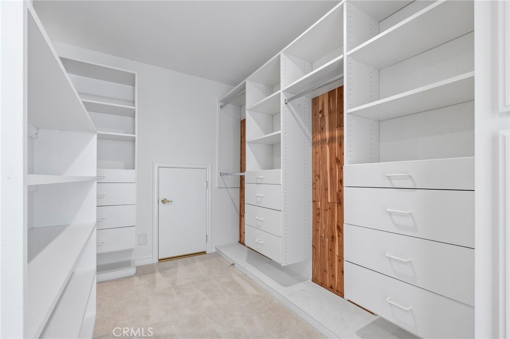 Walk-in closet with white built-in shelving, drawers, and warm wood cabinet panels.