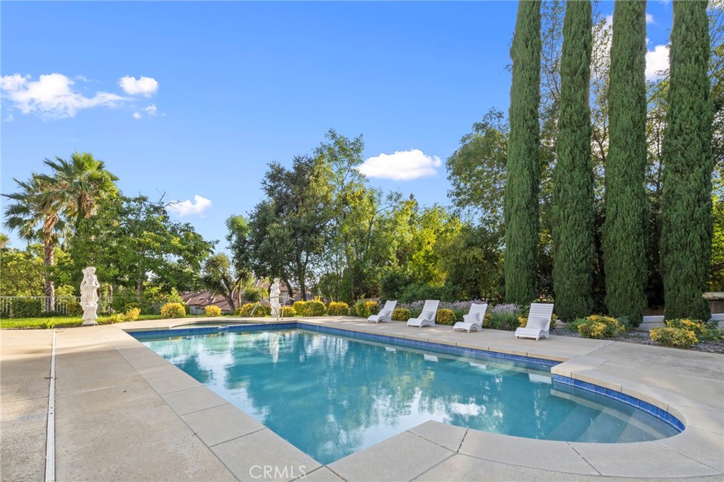Swimming pool with white loungers, a garden statue, and tall cypress trees.