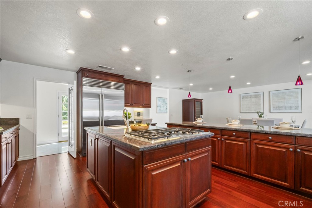 Kitchen with a granite island and gas cooktop, dark wood cabinets, and stainless steel refrigerator.