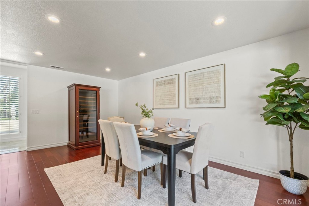 Dining room with a set table, upholstered chairs, glass-front cabinet, and potted tree.