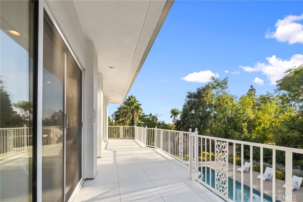 Covered tiled balcony overlooking a swimming pool and leafy trees.