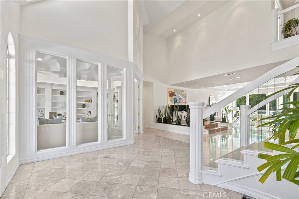 Bright double-height foyer with glossy tile floors and a white staircase with glass railing.