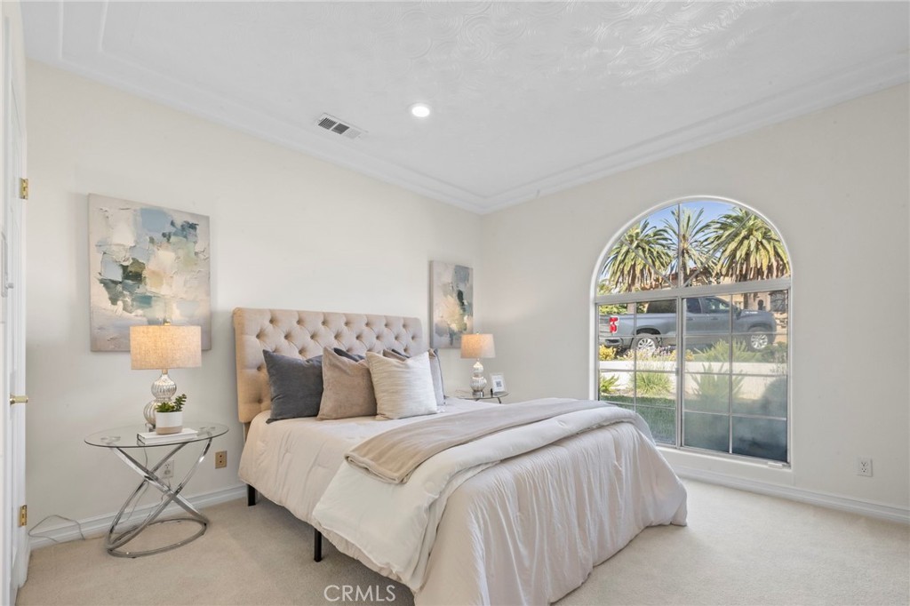 Staged bedroom with a tufted bed and large arched window overlooking palm trees.