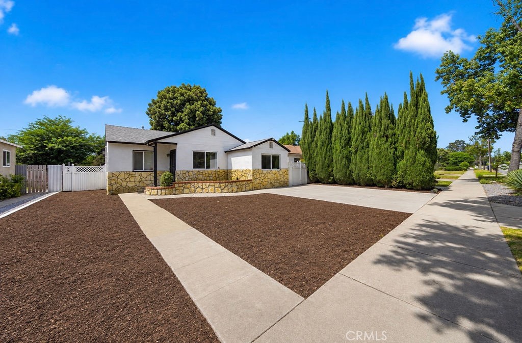 Single-story white house with stone facade, concrete walkway, and tall evergreen trees along the yard.