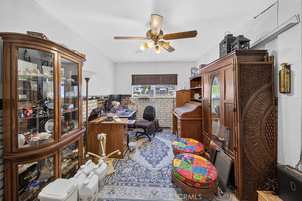 Furnished home office with antique display cabinets, a desk, patterned rug, and colorful stools.