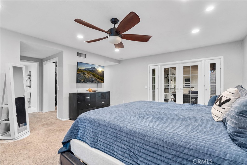 Furnished bedroom with a blue-quilted bed, ceiling fan, and white French doors.