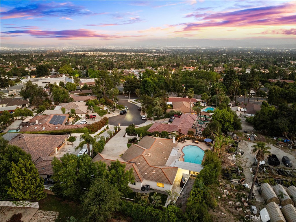 Aerial view of a red-tile-roofed home with a turquoise pool and suburban surroundings at sunset.