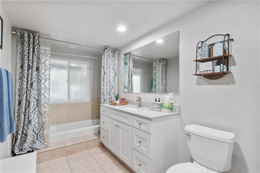Bathroom with a white vanity and large mirror beside a tub with patterned curtains.