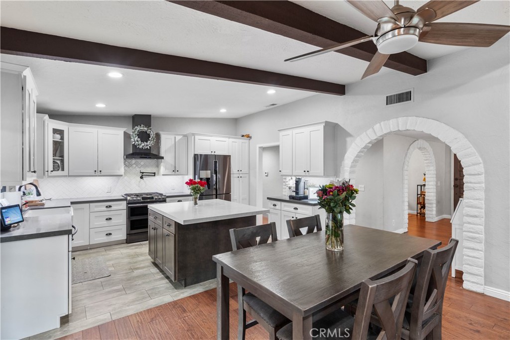 Kitchen and dining area with a large island, white cabinetry, dark wood table, and arched doorway.