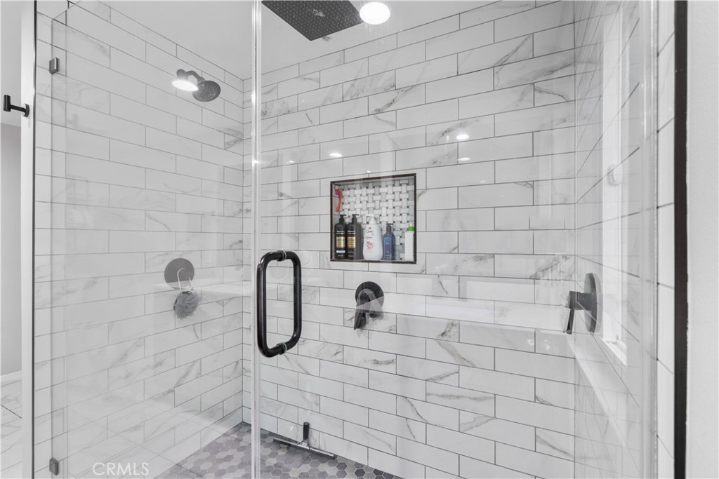 Walk-in shower with marble-look tile, dark fixtures, a built-in niche, and mosaic flooring.