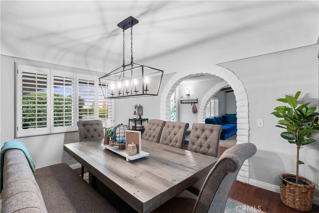 Dining room with a rustic wood table and upholstered chairs beside an arched opening to the living room.