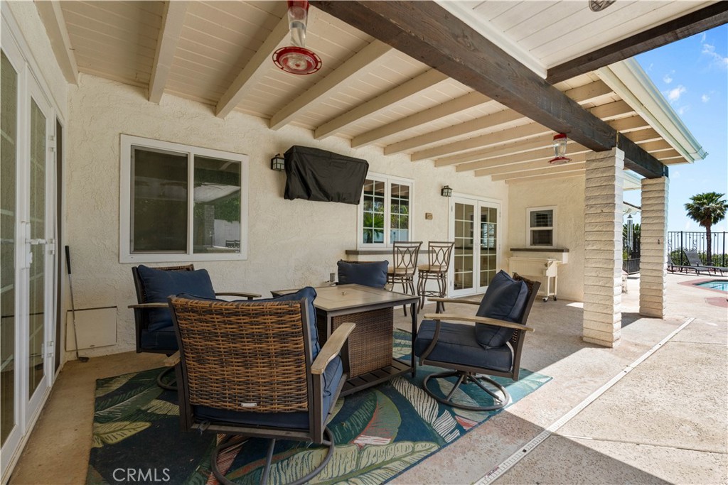 Covered patio with cushioned seating and dining area beside a swimming pool.