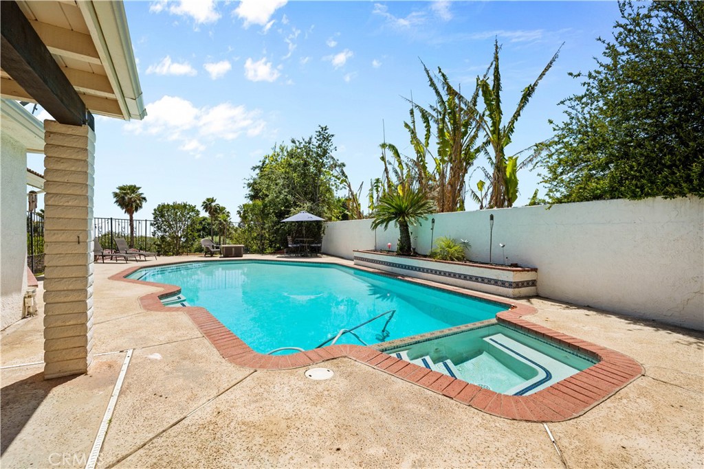 Backyard swimming pool with attached spa, brick edging, and tropical landscaping.