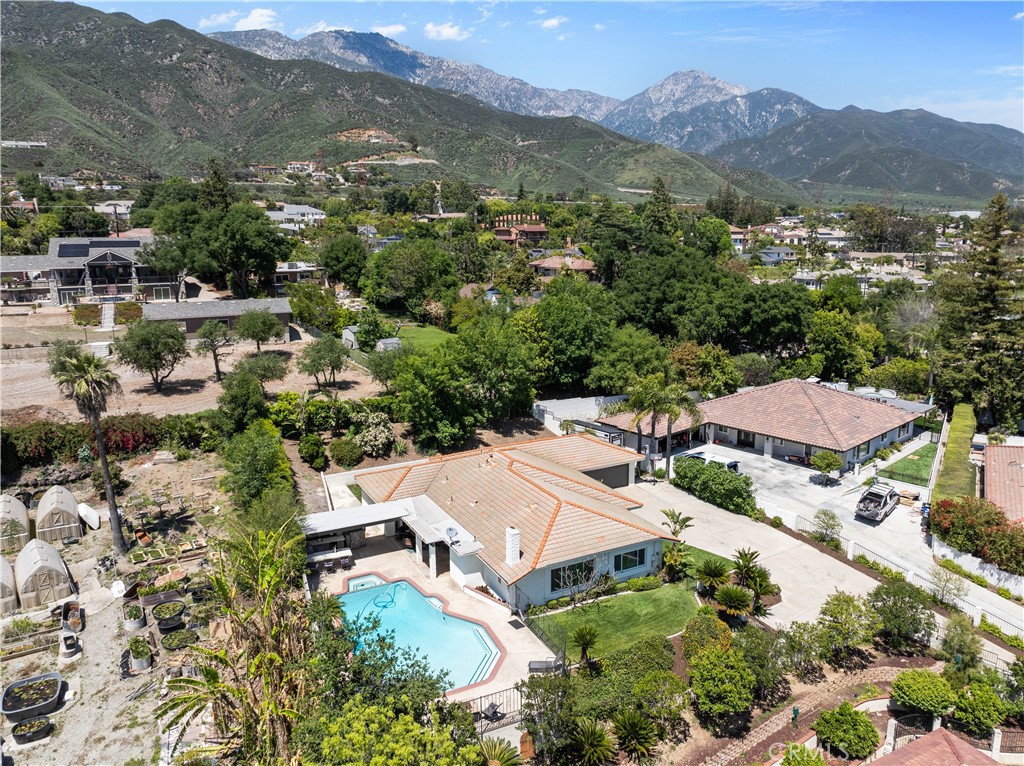 Aerial view of a home with a swimming pool, gardens, and mountains beyond.