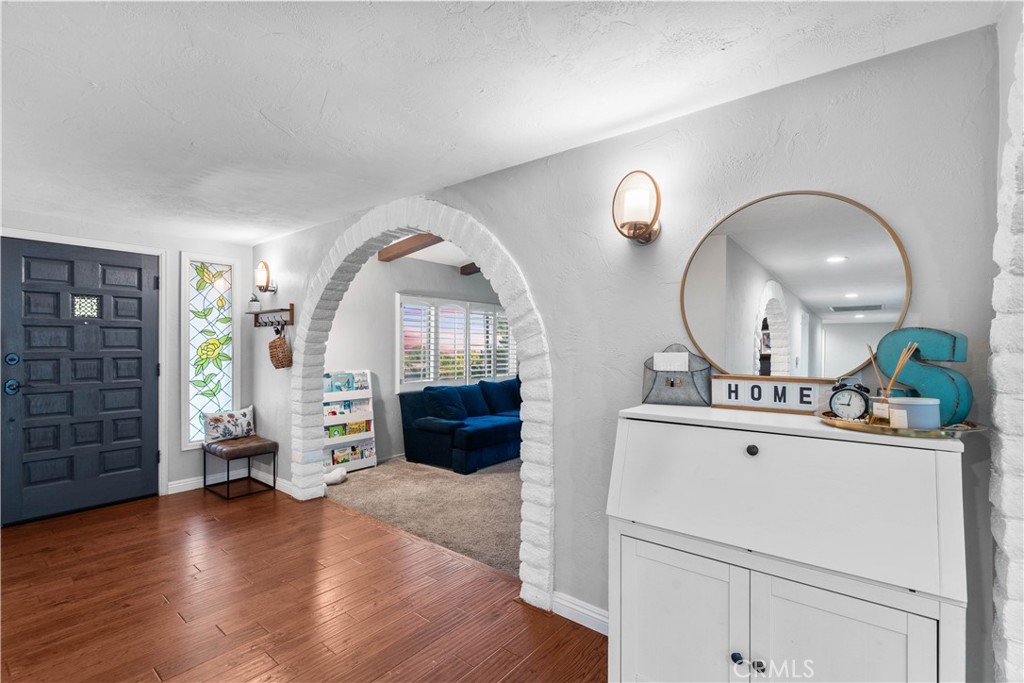 Entryway with a dark paneled door, wood floors, and a stone-trimmed arch framing a blue living room sofa.