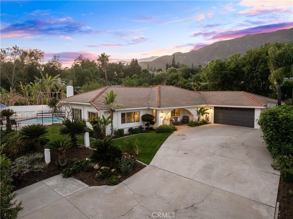 Single-story home with a tiled roof, swimming pool, and broad driveway beneath a colorful dusk sky.