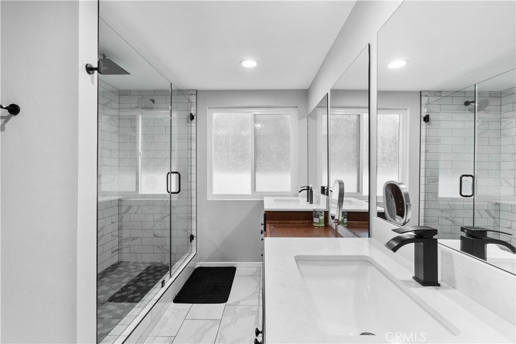 Bathroom with a frameless glass shower, marble-look tile, and a white vanity with a black faucet.