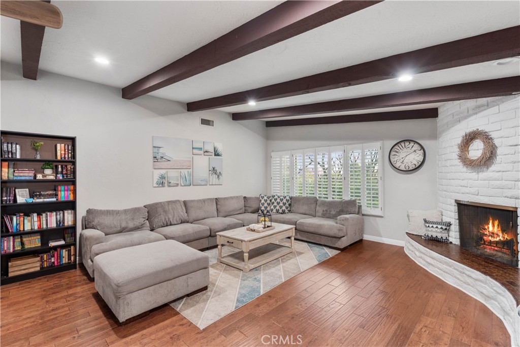 Living room with exposed beams, a gray sectional, and a white brick fireplace.