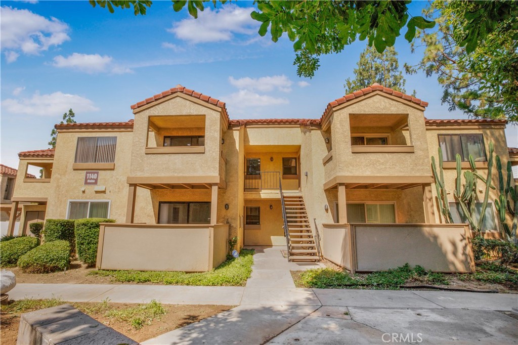 Two-story stucco residential building with terracotta roof tiles, recessed balconies, and a central staircase.