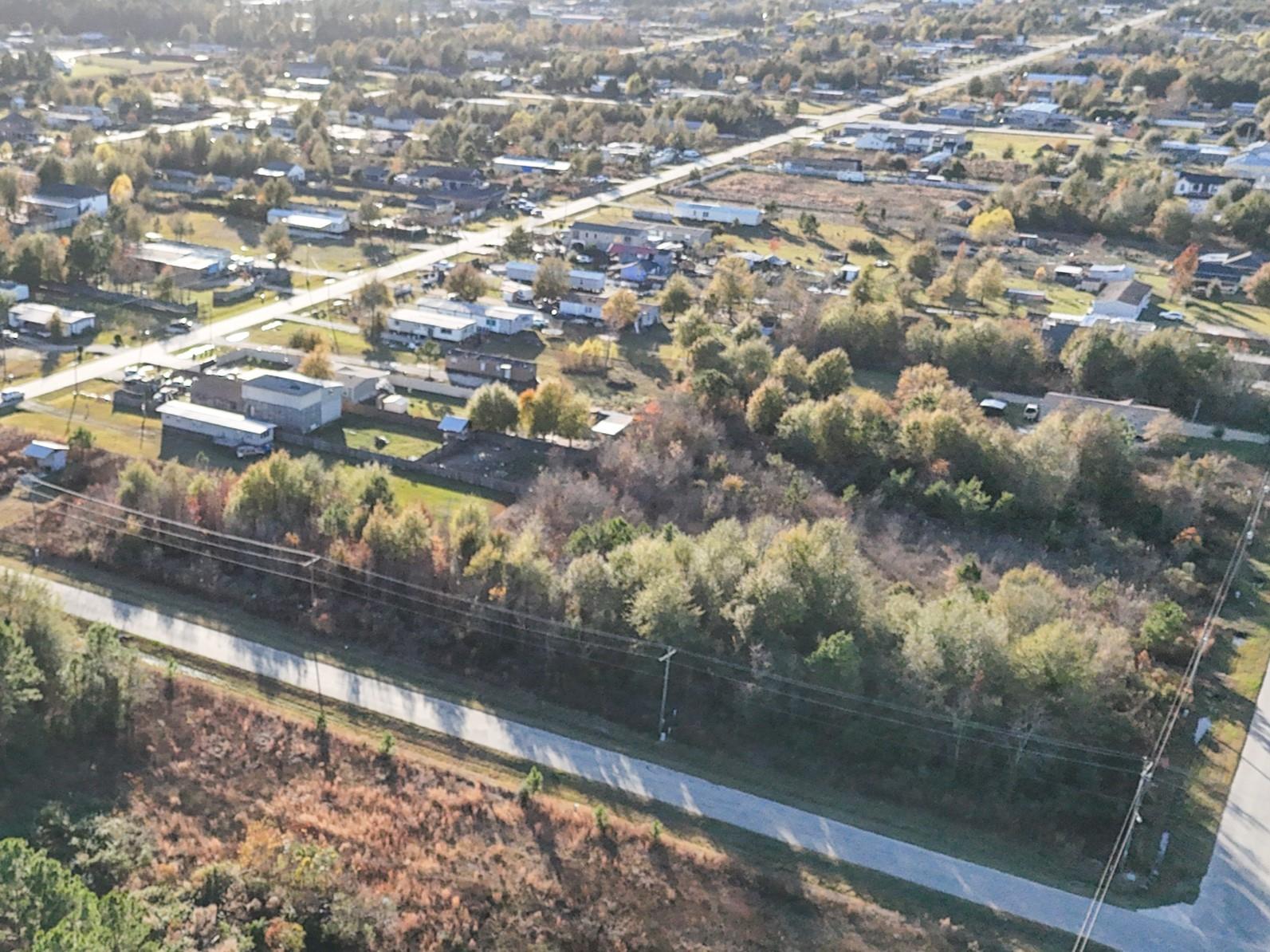 Aerial view of scattered homes and roads beside a wooded, undeveloped parcel.