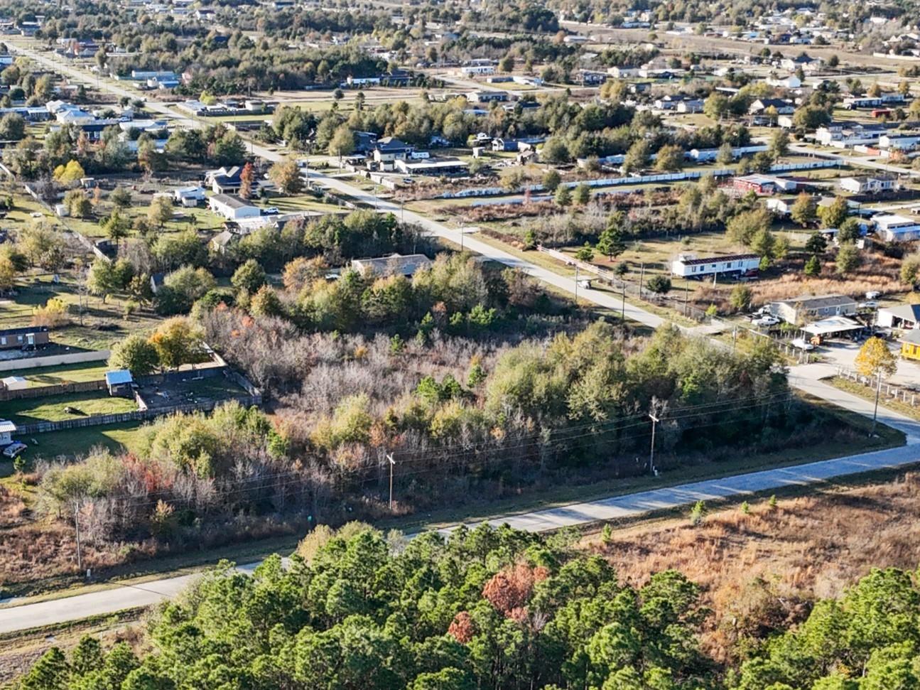 Aerial view of a wooded vacant lot bordered by roads, with homes nearby.