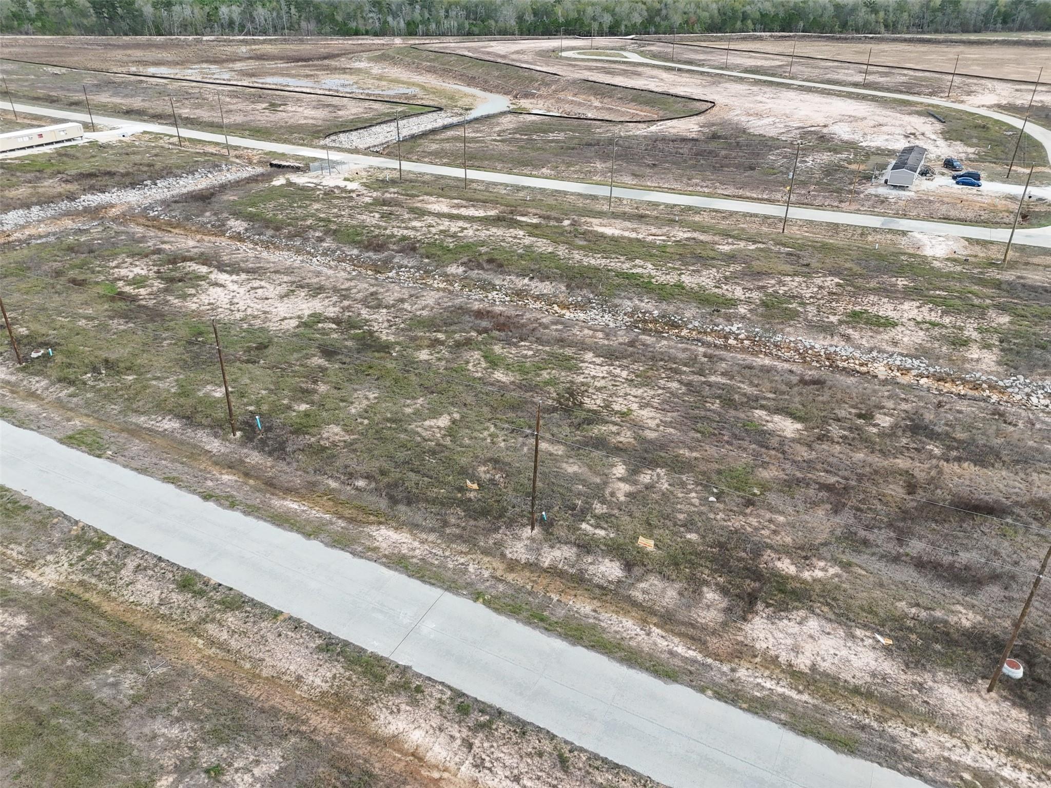 Aerial view of a vacant, patchy-grass parcel beside a paved road, with utility poles and cleared lots nearby.