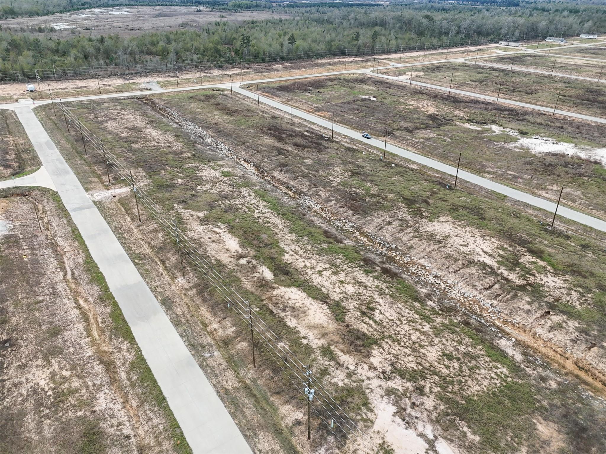 Aerial view of vacant subdivision lots with concrete roads, utility poles, and a rock-lined drainage channel.