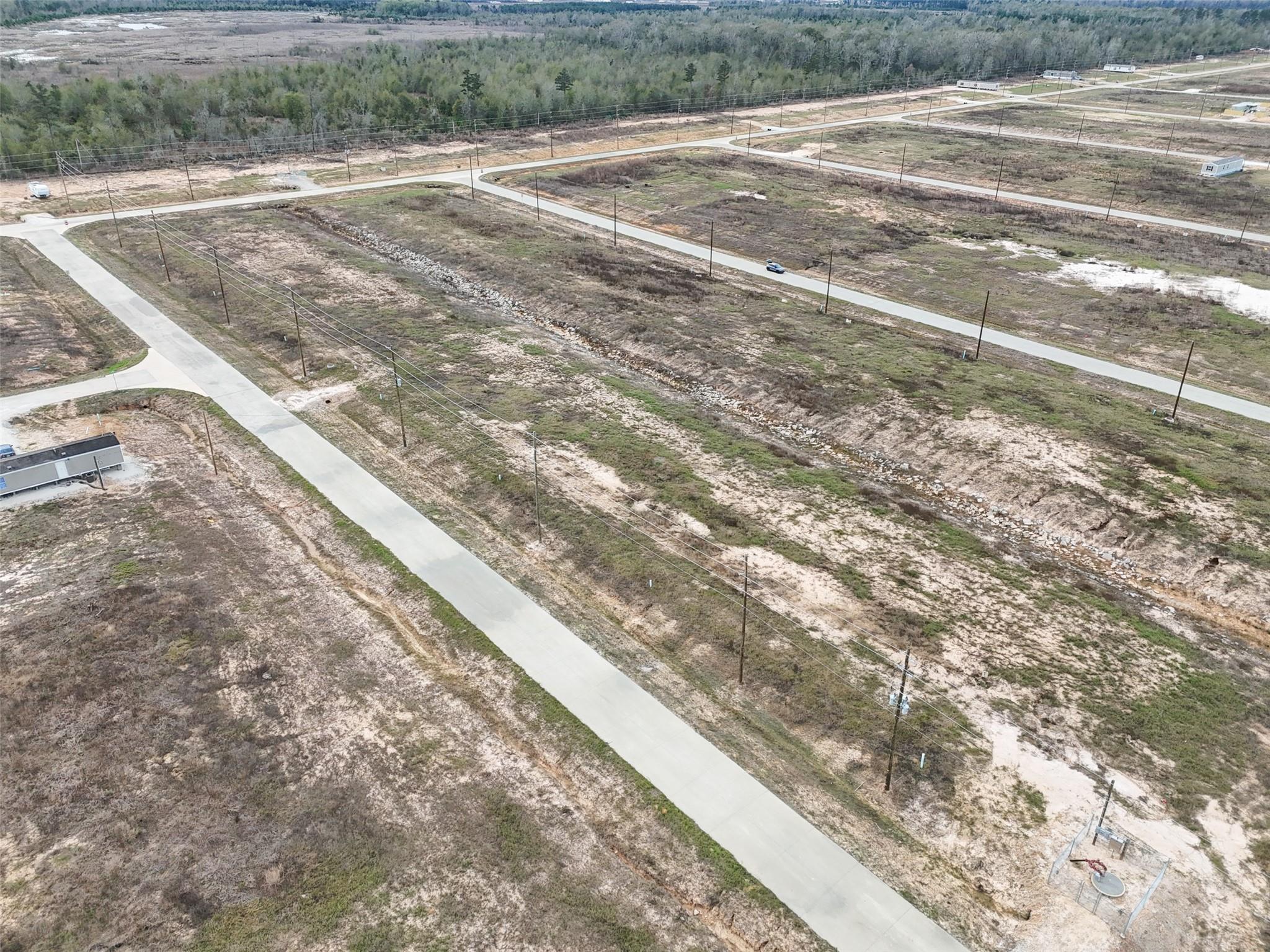 Aerial view of cleared lots and paved roads, with a drainage ditch and woods beyond.