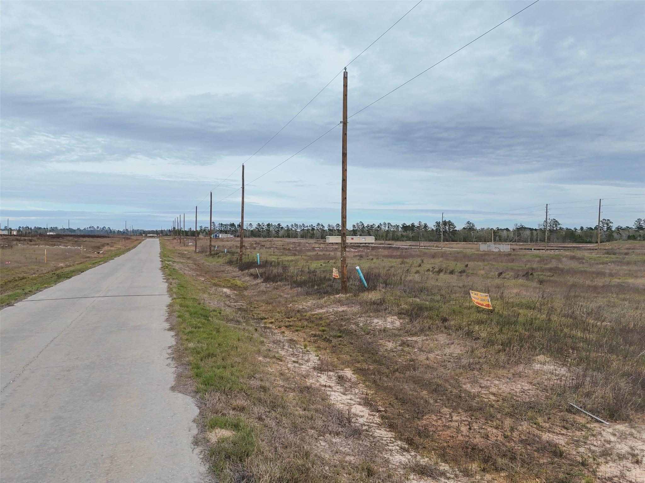 Vacant land beside a paved road, with utility poles and open grassy fields.