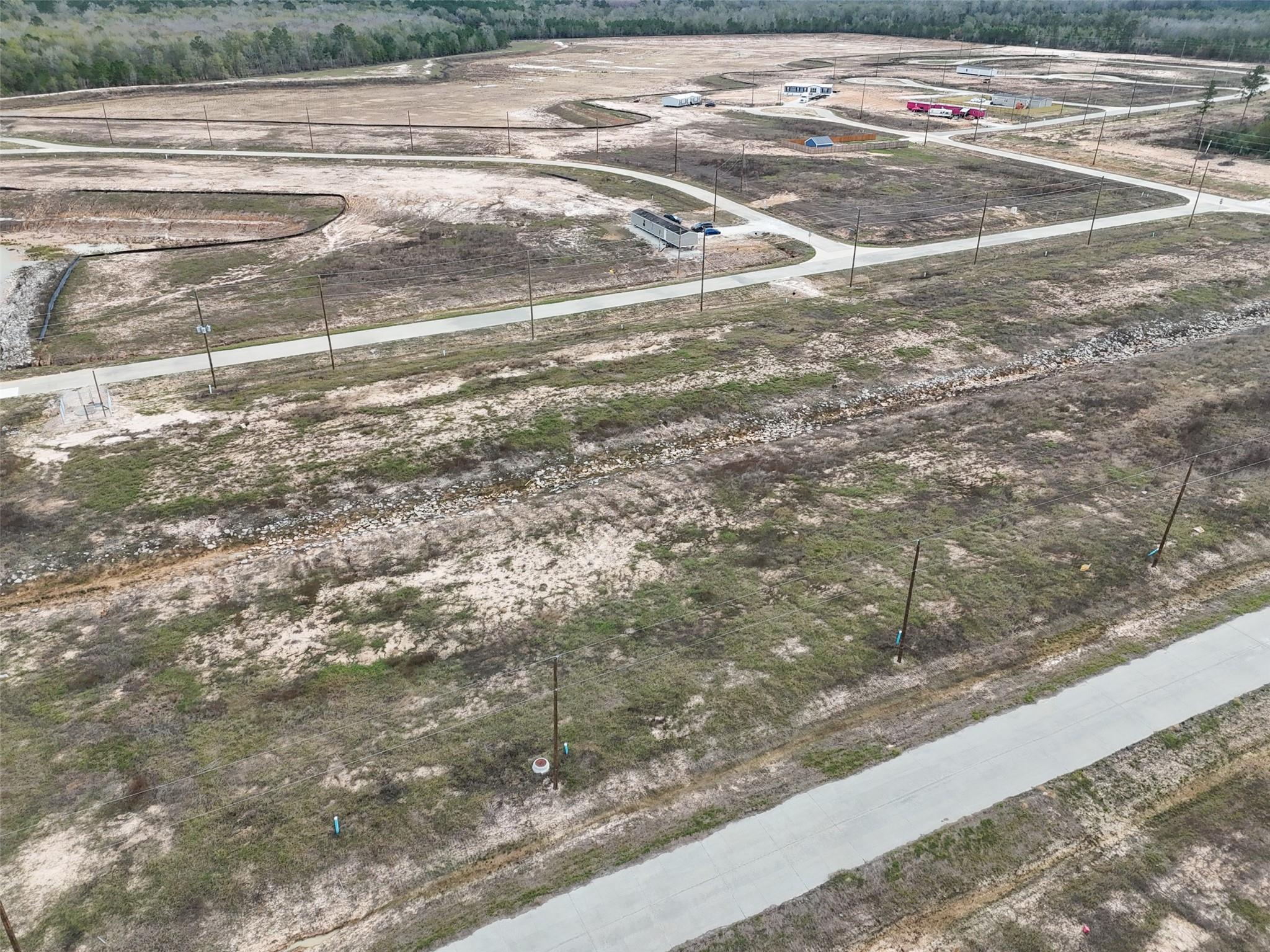 Aerial view of sandy vacant lots and new roads, with utility poles and woods in the distance.