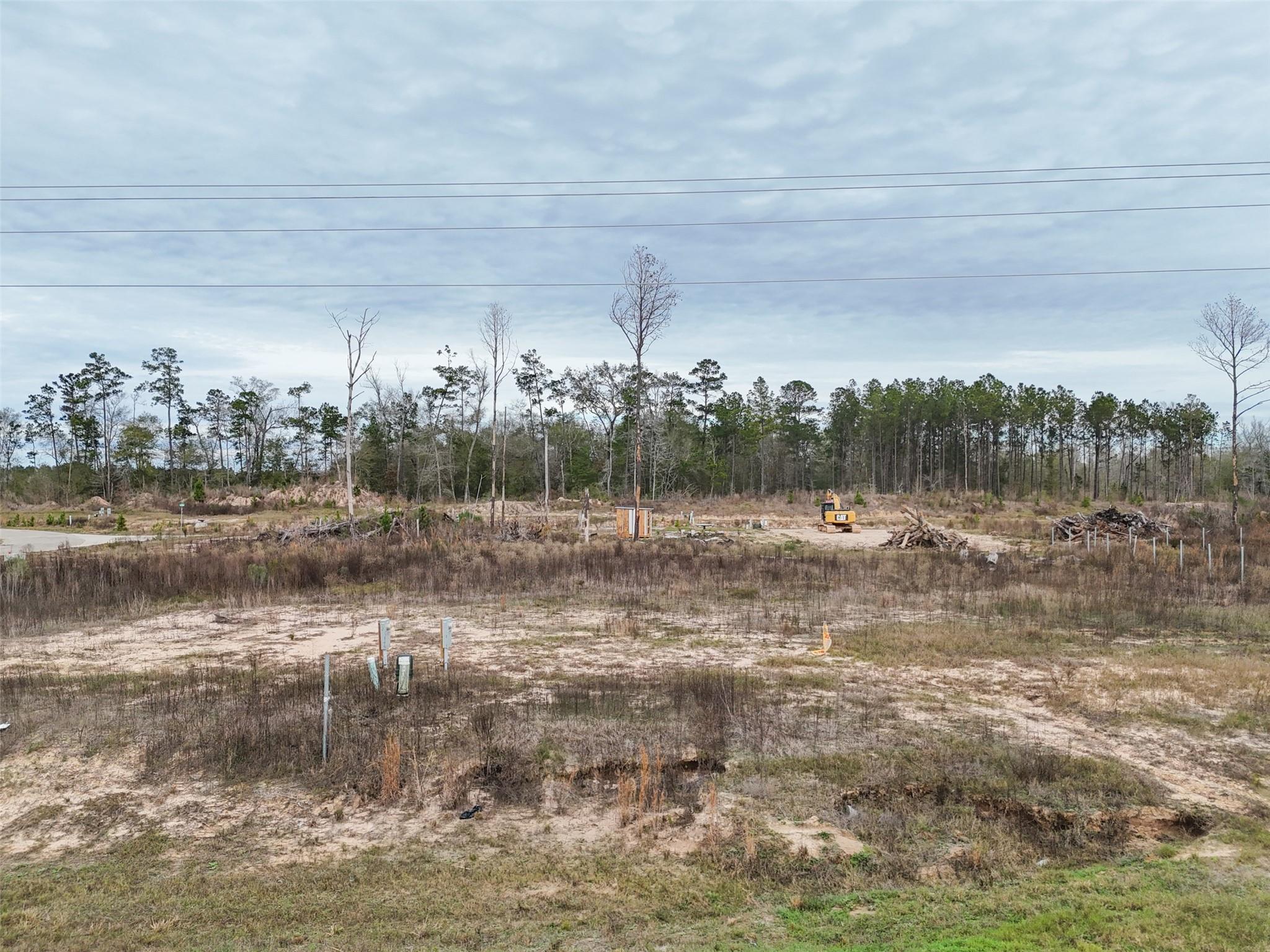 Cleared vacant lot with sandy ground, utility markers, brush piles, and a CAT machine near the tree line.