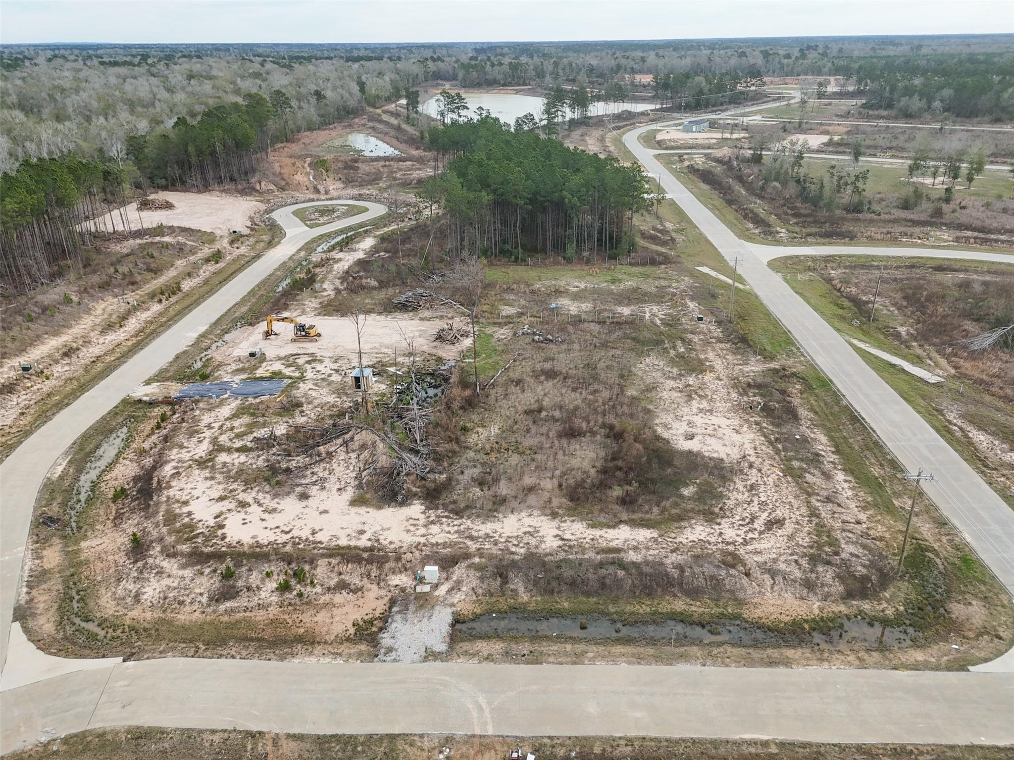 Aerial view of a cleared vacant lot beside new paved roads, with woods and ponds nearby.
