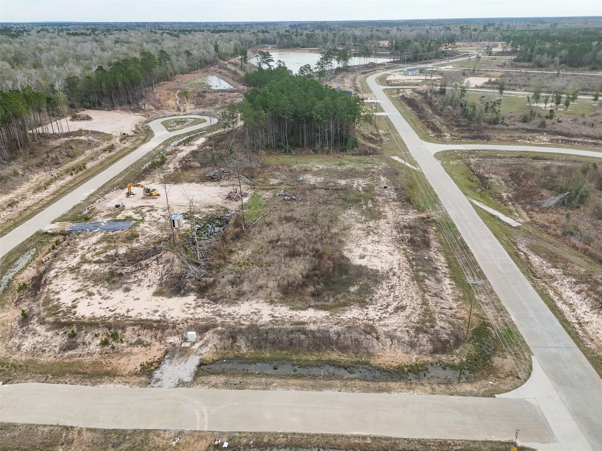 Aerial view of a sandy vacant lot beside new paved subdivision roads and wooded areas.