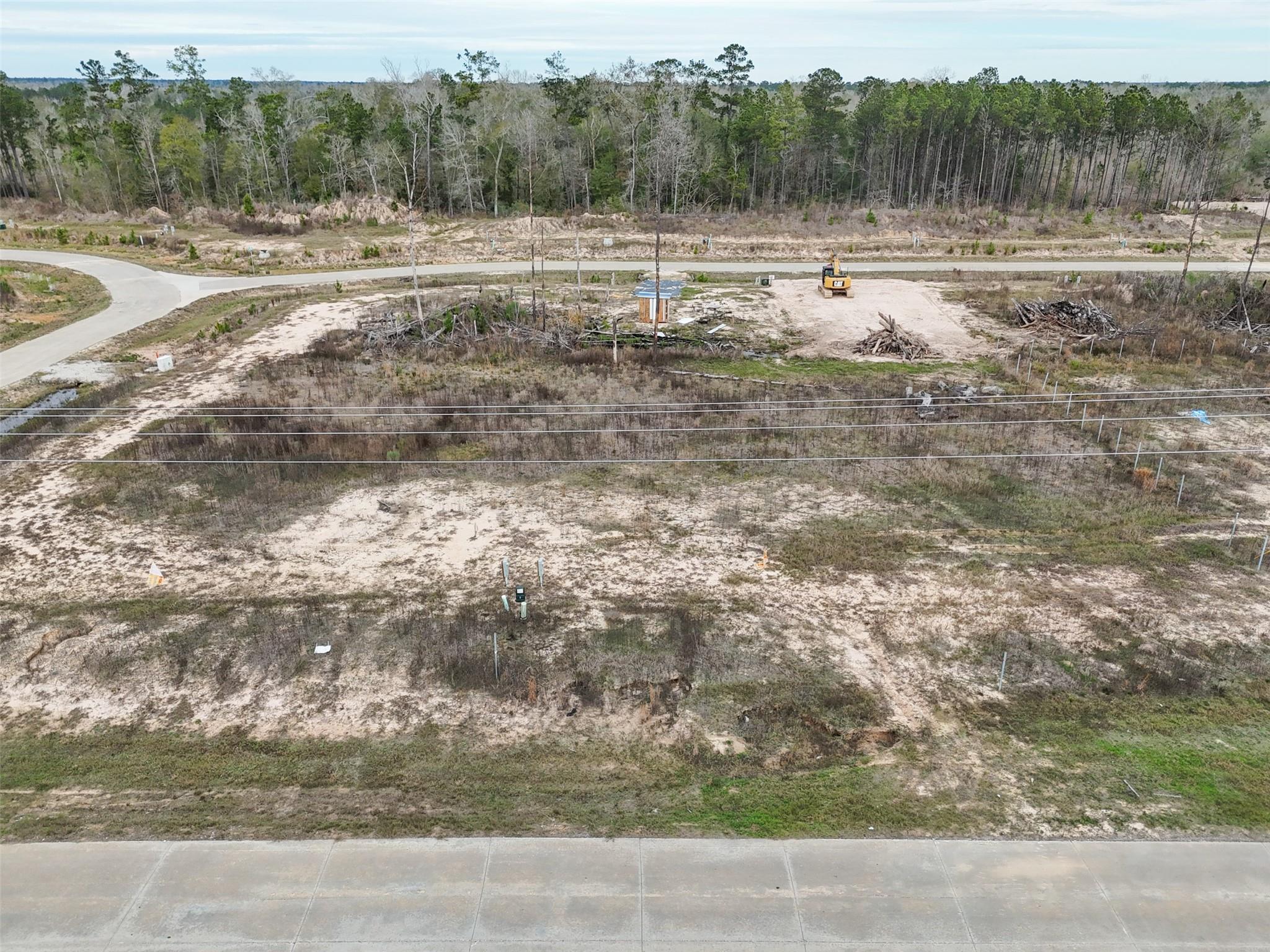 Aerial view of a cleared vacant lot with utility lines and an excavator near the road.