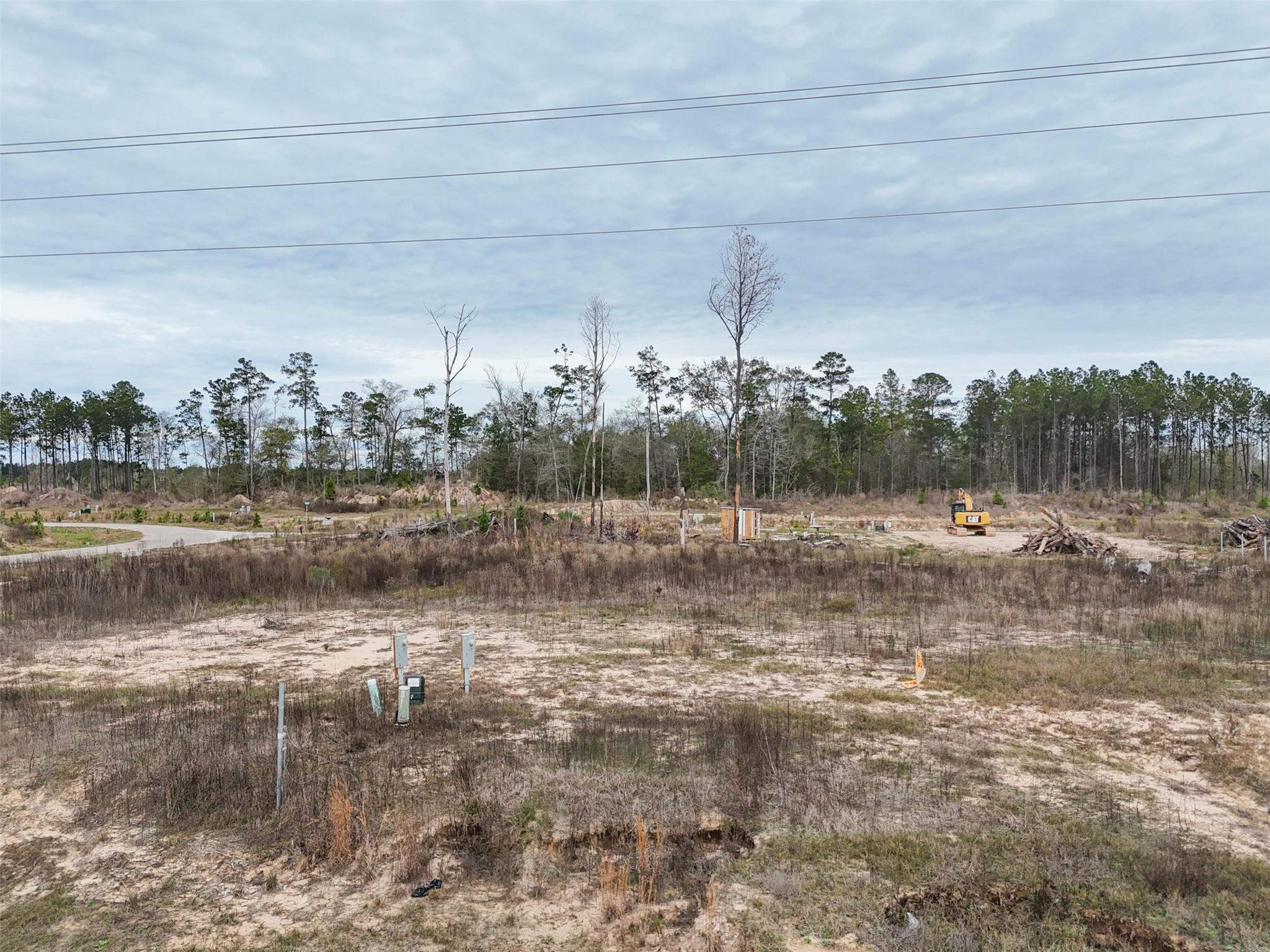 Cleared sandy lot with utility markers and a small excavator, bordered by trees.