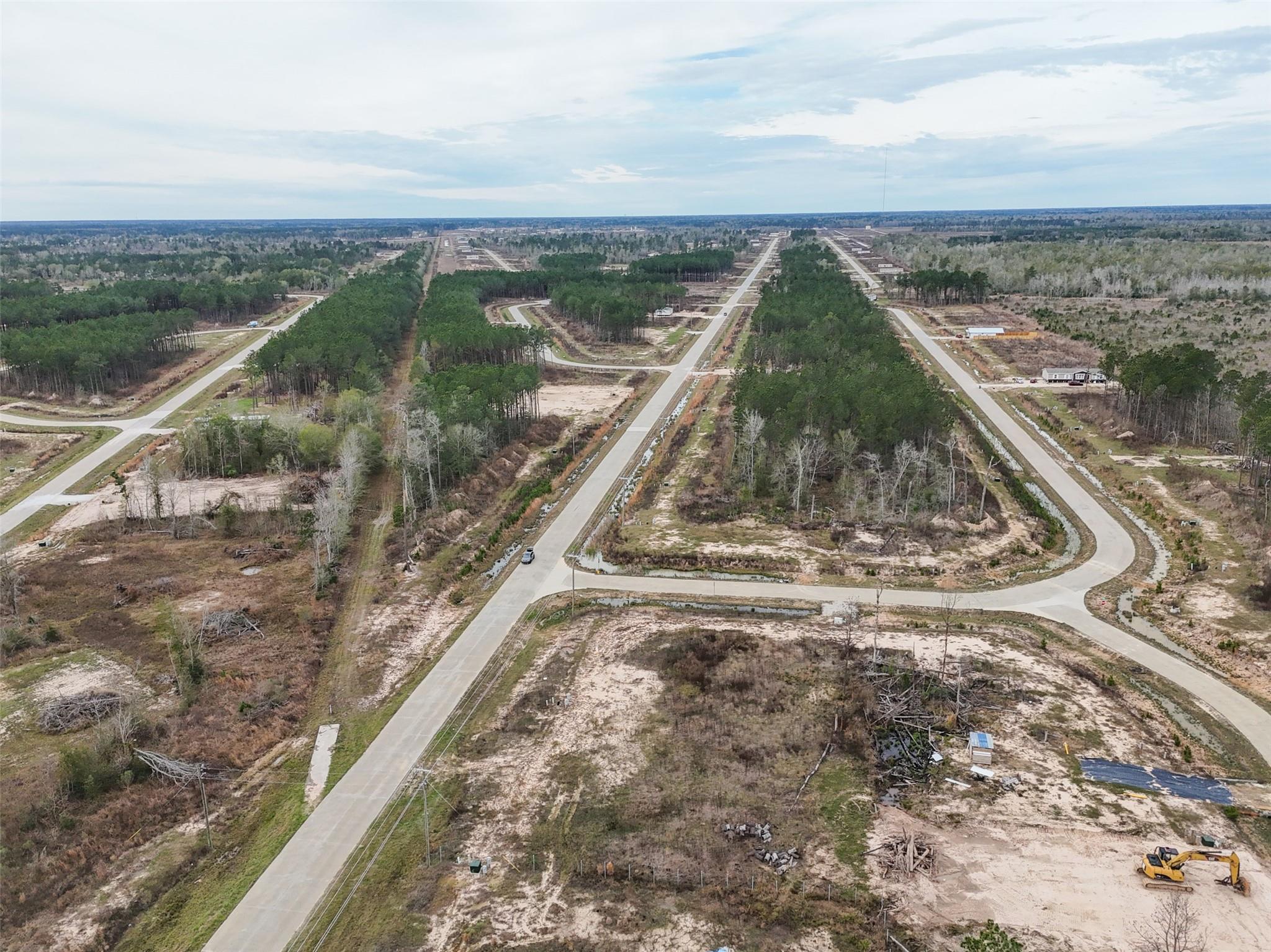 Aerial view of a developing subdivision with winding roads, wooded lots, and an excavator.